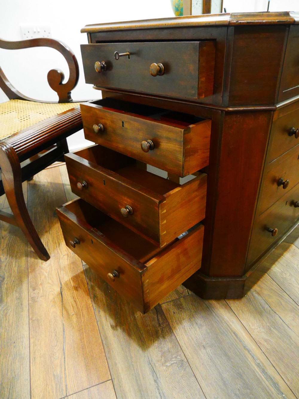 An octagonal Victorian mahogany pedestal desk with multiple drawers featuring turned wood handles and a dark inset leather writing surface. View IV