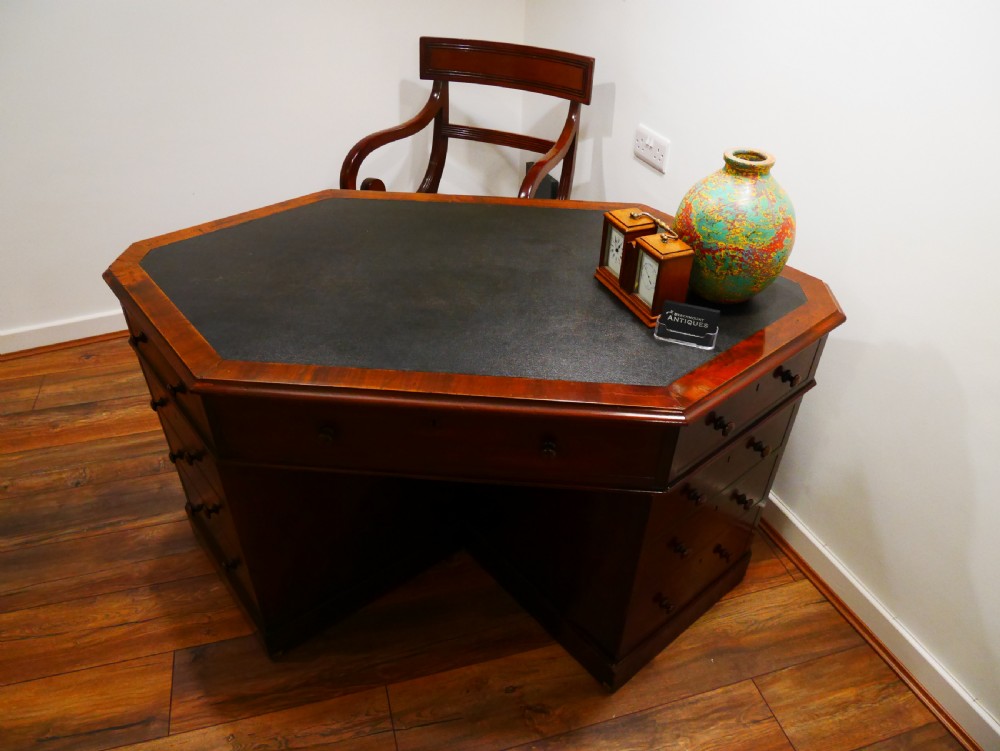 An octagonal Victorian mahogany pedestal desk with multiple drawers featuring turned wood handles and a dark inset leather writing surface. View V