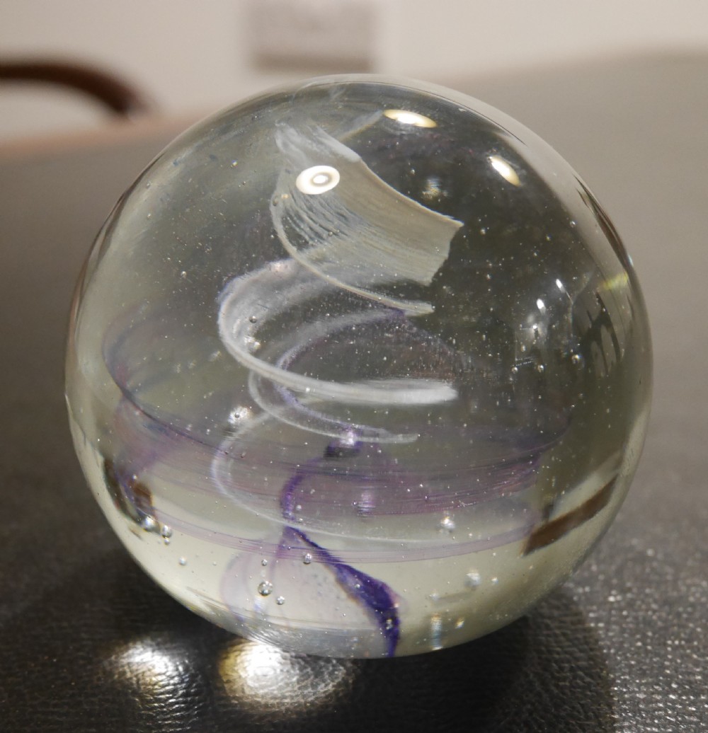 A spherical clear glass paperweight displaying an internal spiral ribbon detail in white and purple with small air bubbles. View II