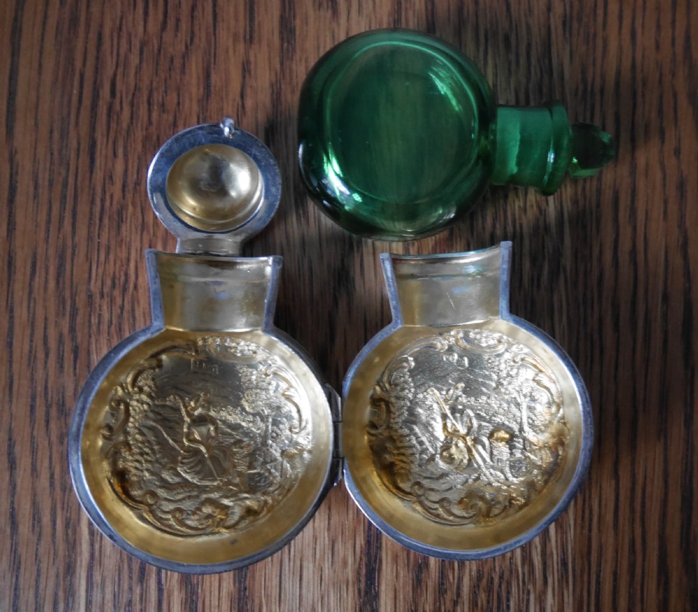 A circular Victorian sterling silver scent bottle decorated with a repousse pastoral scene and topped with a polished silver lid. View II