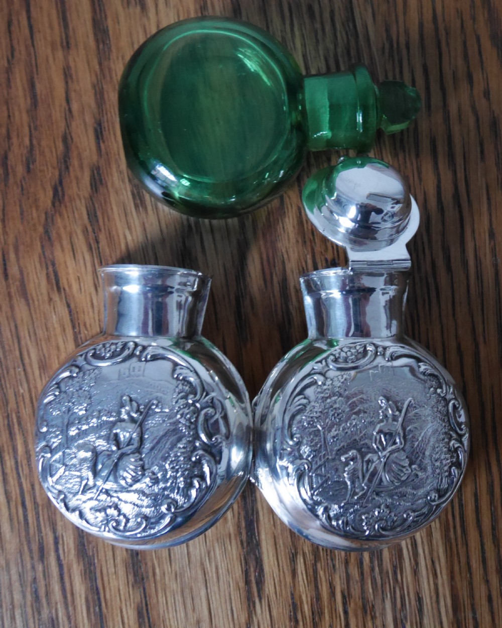 A circular Victorian sterling silver scent bottle decorated with a repousse pastoral scene and topped with a polished silver lid. View III