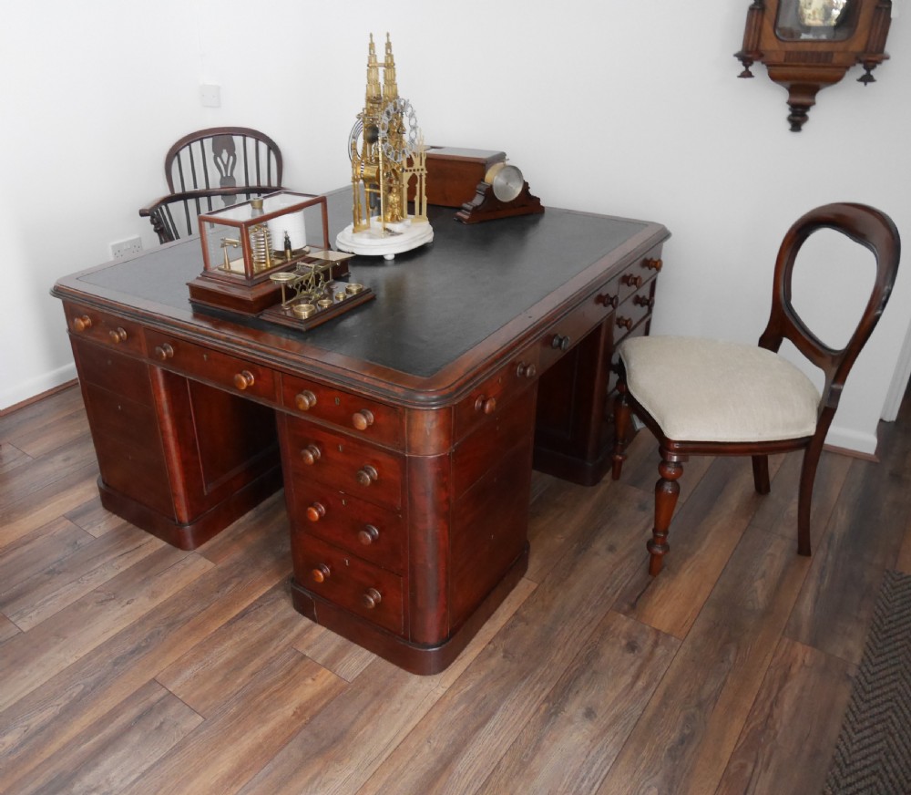 A 19th-century mahogany four-pedestal partners desk with a dark leather top, multiple drawers, and turned wooden knobs. View V