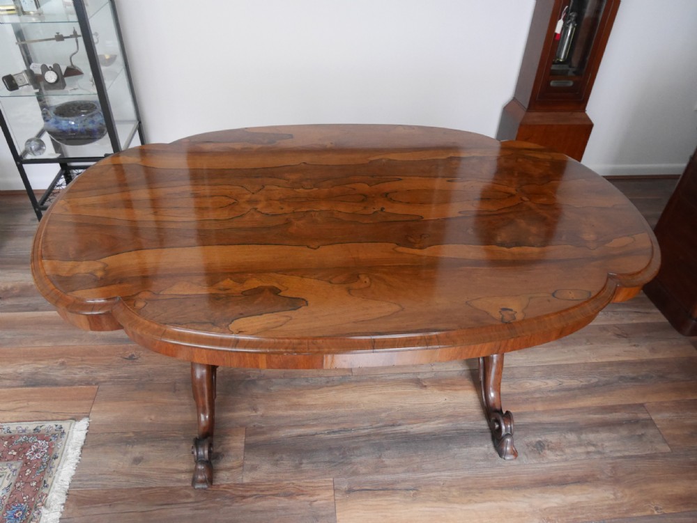 An antique Victorian rosewood centre table featuring a polished serpentine shaped top with prominent wood graining and carved scroll feet.