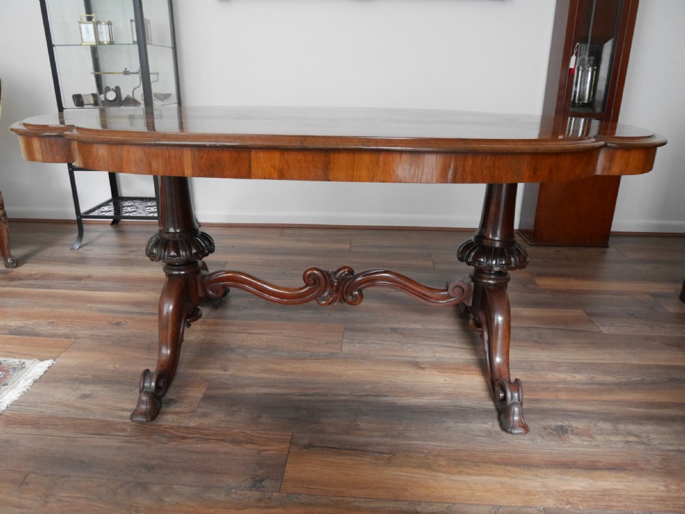 An antique Victorian rosewood centre table featuring a polished serpentine shaped top with prominent wood graining and carved scroll feet. View III