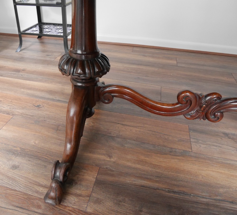An antique Victorian rosewood centre table featuring a polished serpentine shaped top with prominent wood graining and carved scroll feet. View IV
