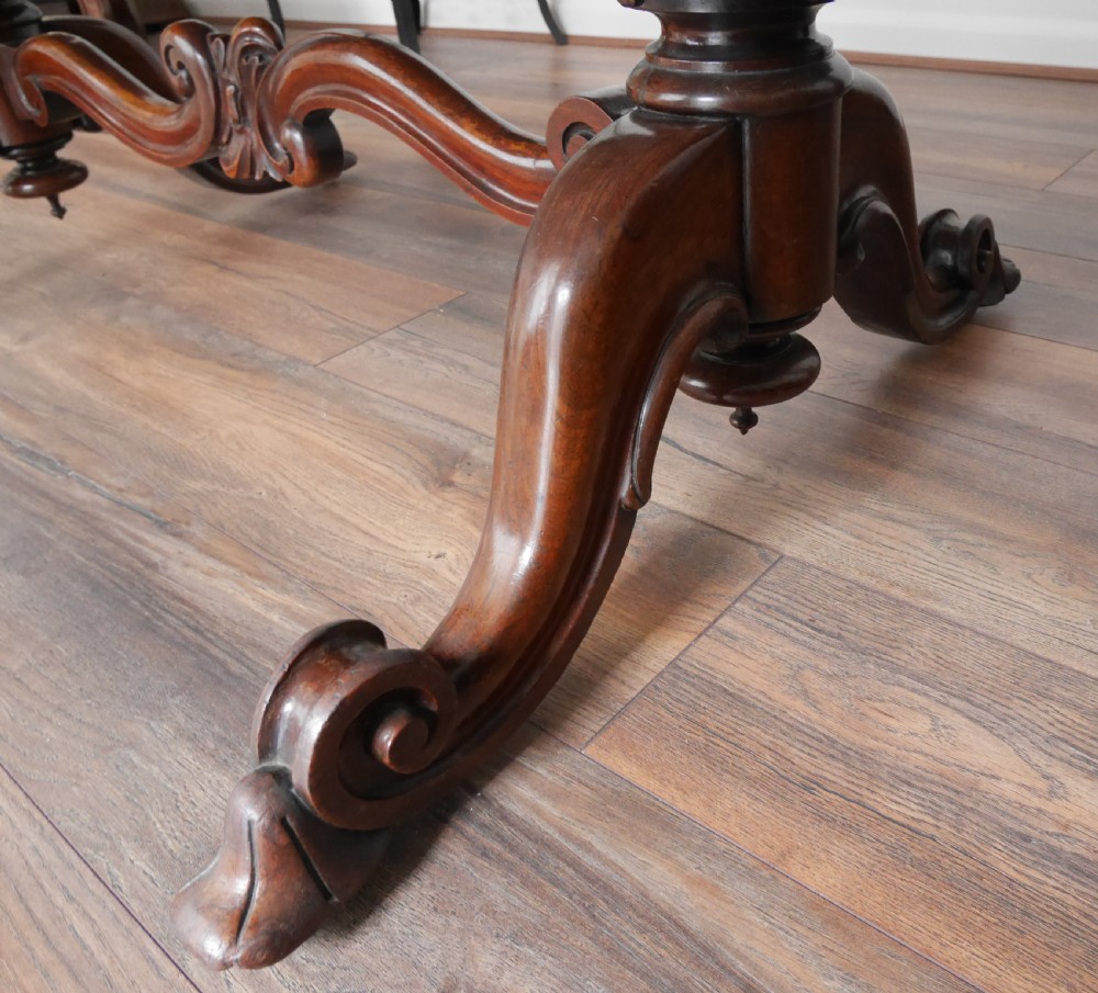 An antique Victorian rosewood centre table featuring a polished serpentine shaped top with prominent wood graining and carved scroll feet. View V
