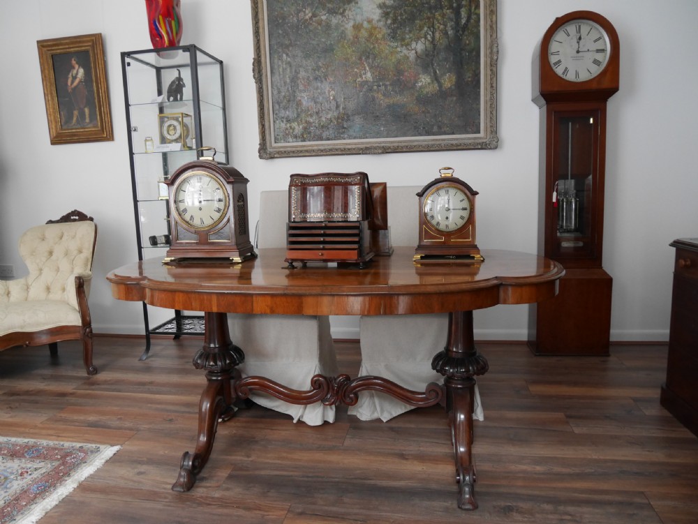 An antique Victorian rosewood centre table featuring a polished serpentine shaped top with prominent wood graining and carved scroll feet. View VI