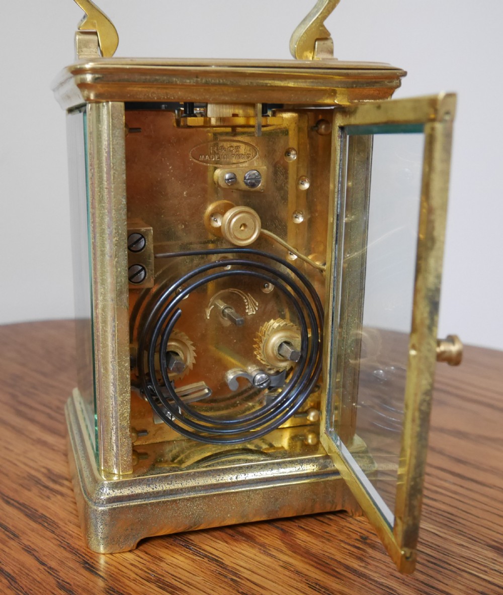 An antique brass carriage clock featuring a top carrying handle, glass side panels, and a white enamel dial with black Roman numerals. View III