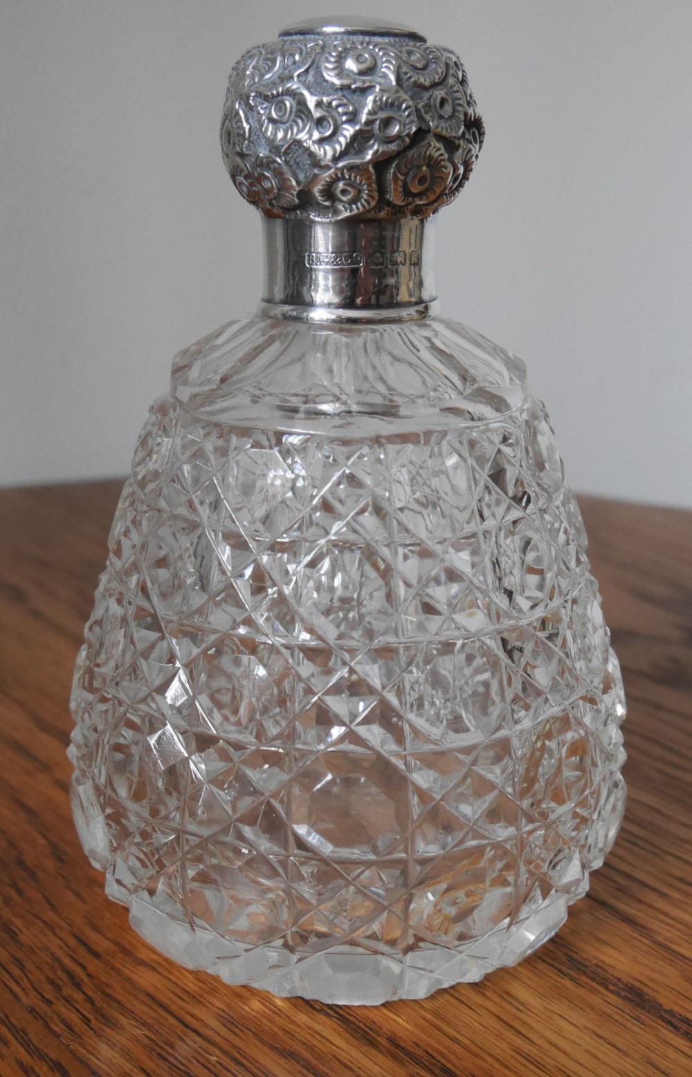 A clear cut-glass scent bottle with a diamond-patterned reservoir and an embossed, hallmarked sterling silver top.