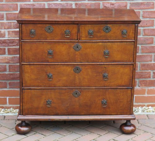 fig 2. An early 18th-century Queen Anne period walnut chest of drawers featuring two short drawers over three long drawers, standing on turned bun feet.