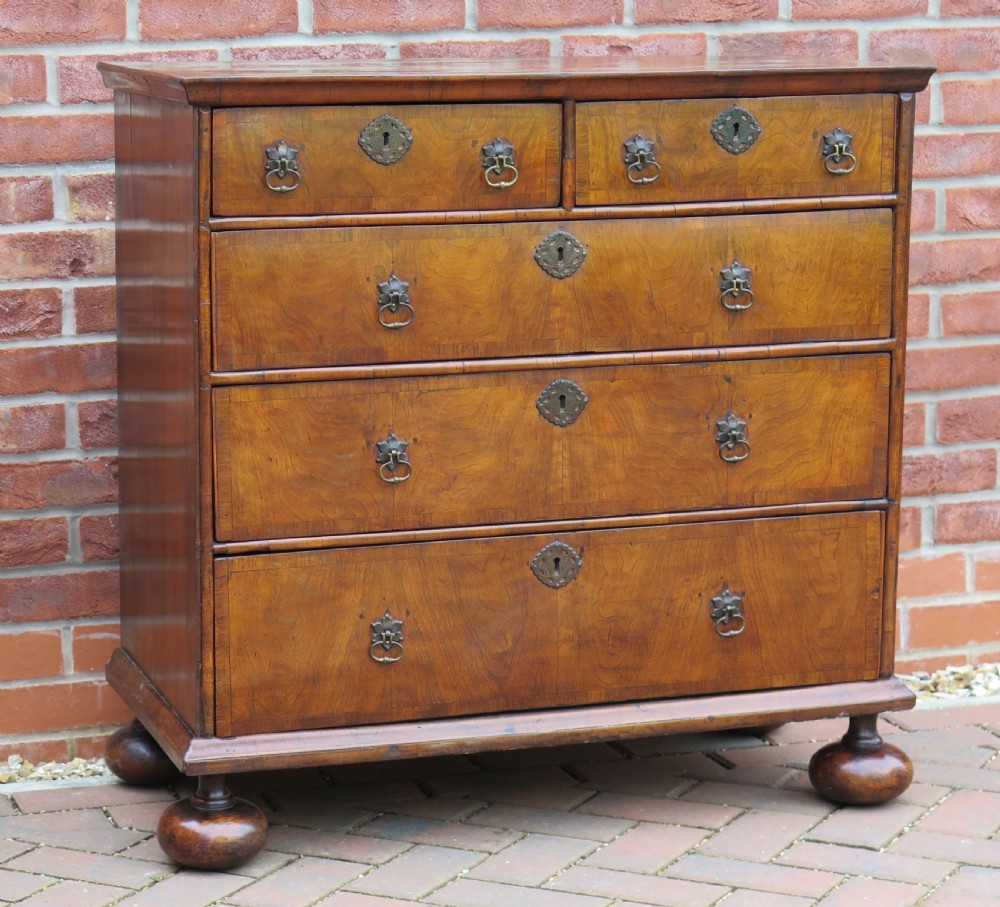 An early 18th-century Queen Anne period walnut chest of drawers featuring two short drawers over three long drawers, standing on turned bun feet.