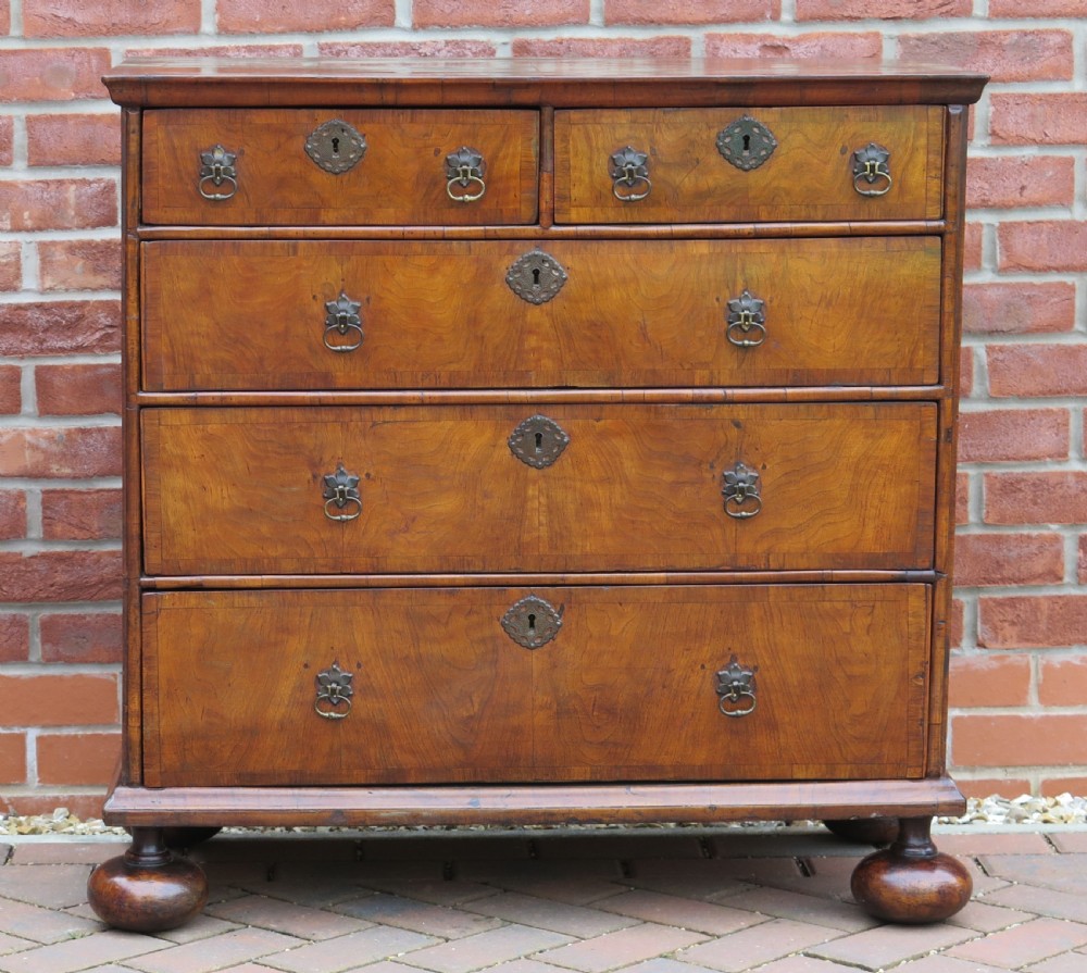 An early 18th-century Queen Anne period walnut chest of drawers featuring two short drawers over three long drawers, standing on turned bun feet. View II