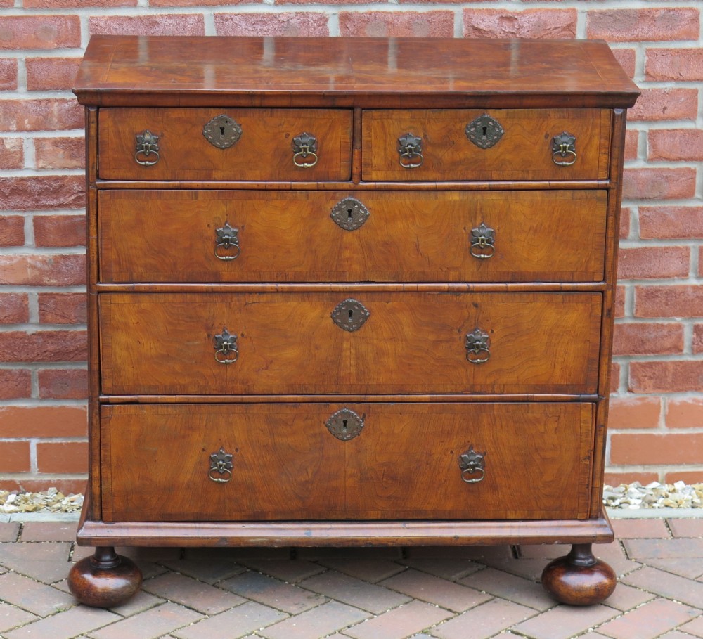 An early 18th-century Queen Anne period walnut chest of drawers featuring two short drawers over three long drawers, standing on turned bun feet. View III