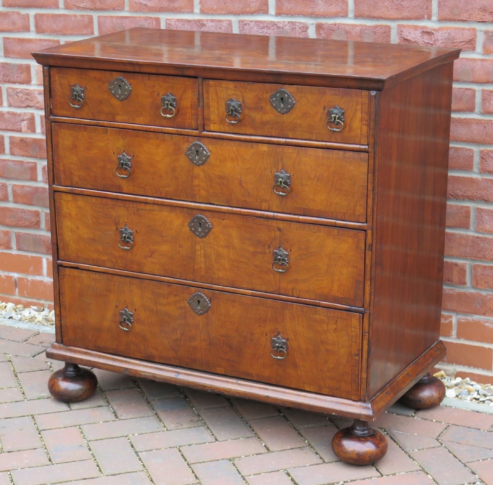 An early 18th-century Queen Anne period walnut chest of drawers featuring two short drawers over three long drawers, standing on turned bun feet. View IV