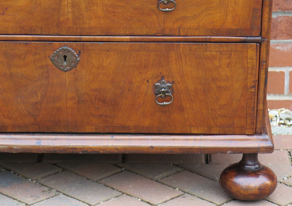 An early 18th-century Queen Anne period walnut chest of drawers featuring two short drawers over three long drawers, standing on turned bun feet. View IX