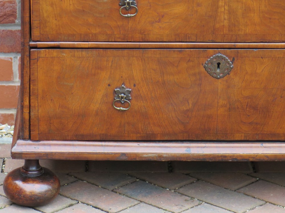An early 18th-century Queen Anne period walnut chest of drawers featuring two short drawers over three long drawers, standing on turned bun feet. View X