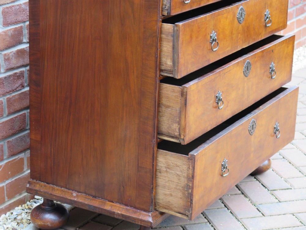 An early 18th-century Queen Anne period walnut chest of drawers featuring two short drawers over three long drawers, standing on turned bun feet. View XIV