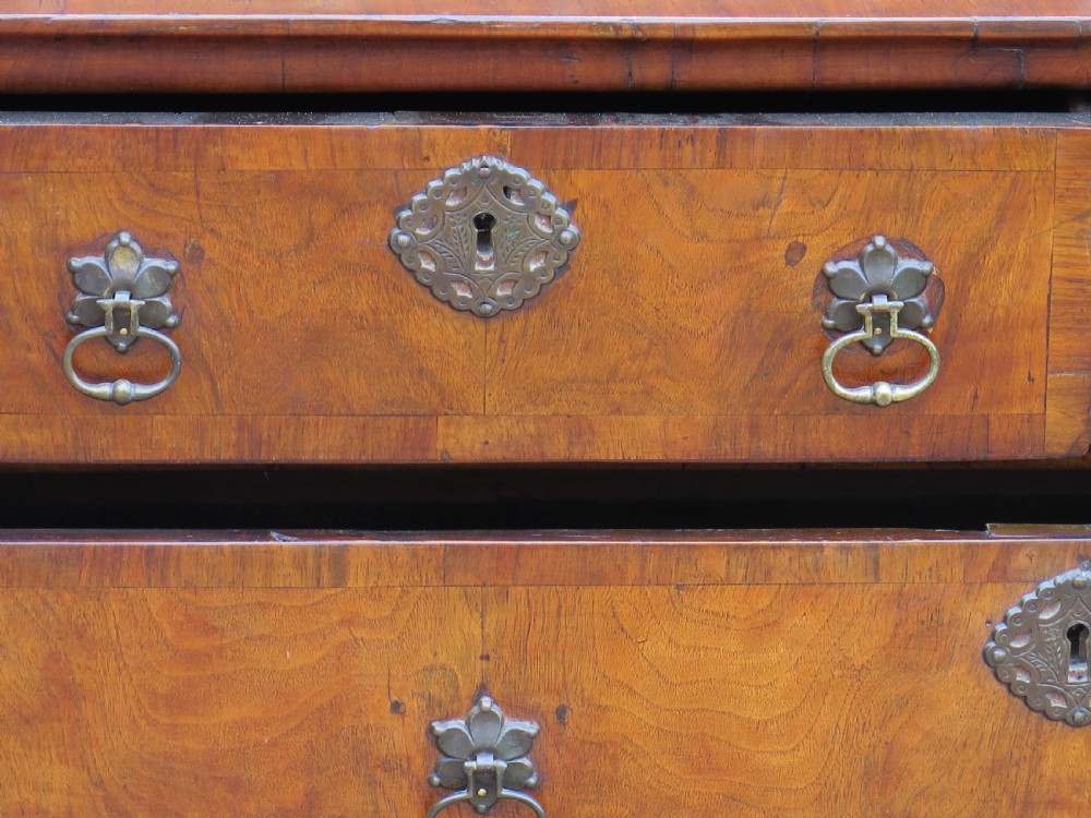 An early 18th-century Queen Anne period walnut chest of drawers featuring two short drawers over three long drawers, standing on turned bun feet. View XVI