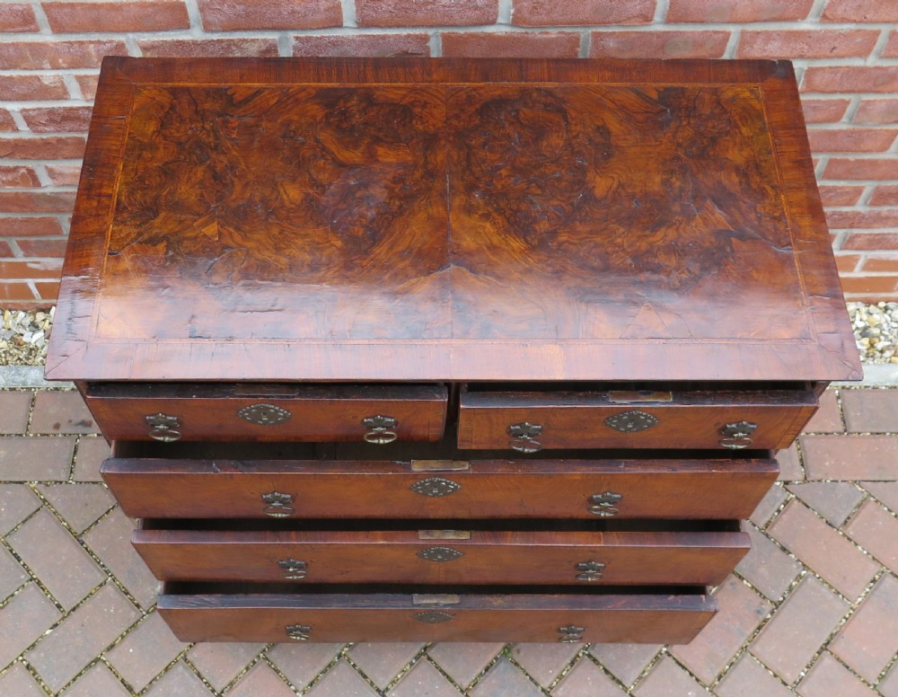 An early 18th-century Queen Anne period walnut chest of drawers featuring two short drawers over three long drawers, standing on turned bun feet. View XVII