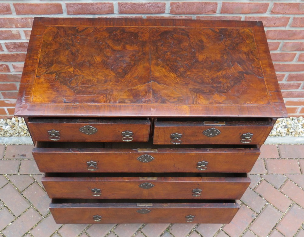 An early 18th-century Queen Anne period walnut chest of drawers featuring two short drawers over three long drawers, standing on turned bun feet. View XVIII