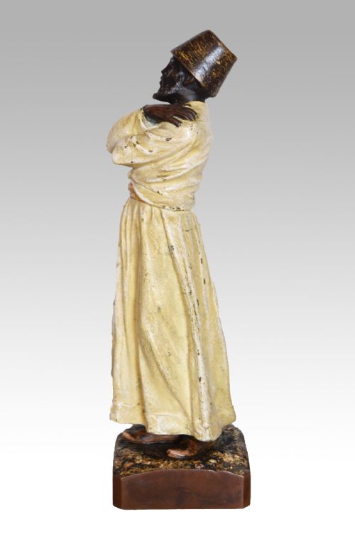 fig 1. A cold-painted bronze sculpture depicting a standing Sufi whirling dervish with arms crossed over a long cream robe, wearing a conical tall hat.