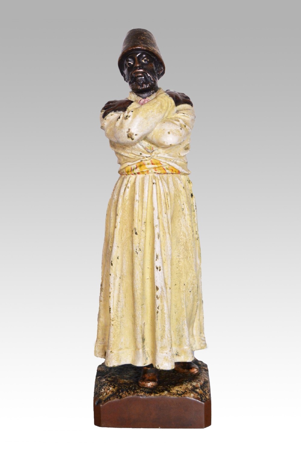 A cold-painted bronze sculpture depicting a standing Sufi whirling dervish with arms crossed over a long cream robe, wearing a conical tall hat.