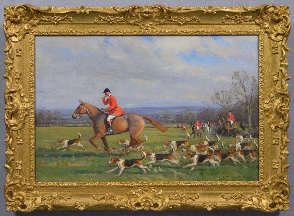 An equestrian oil painting in an ornate gold frame depicting a huntsman in a red coat riding a brown horse alongside a pack of hounds in an open countryside landscape.