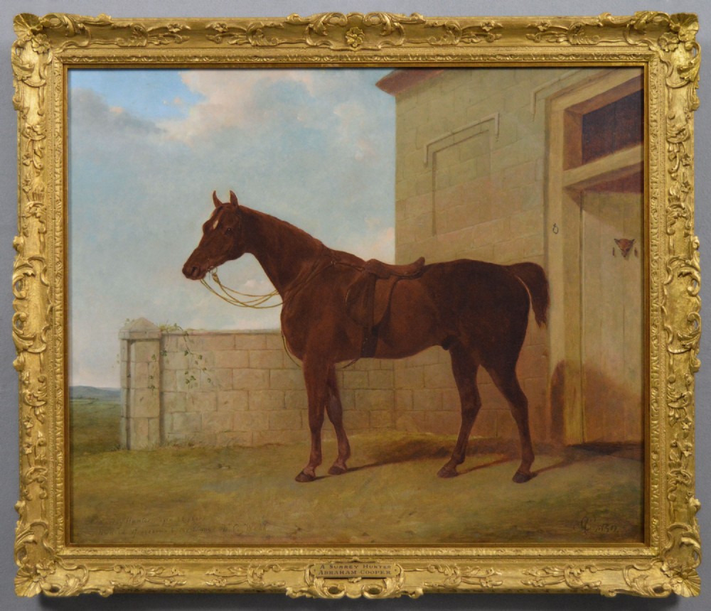 An antique oil painting depicting a saddled chestnut hunter horse standing profile against a stone stable wall within a carved gilt wood frame.