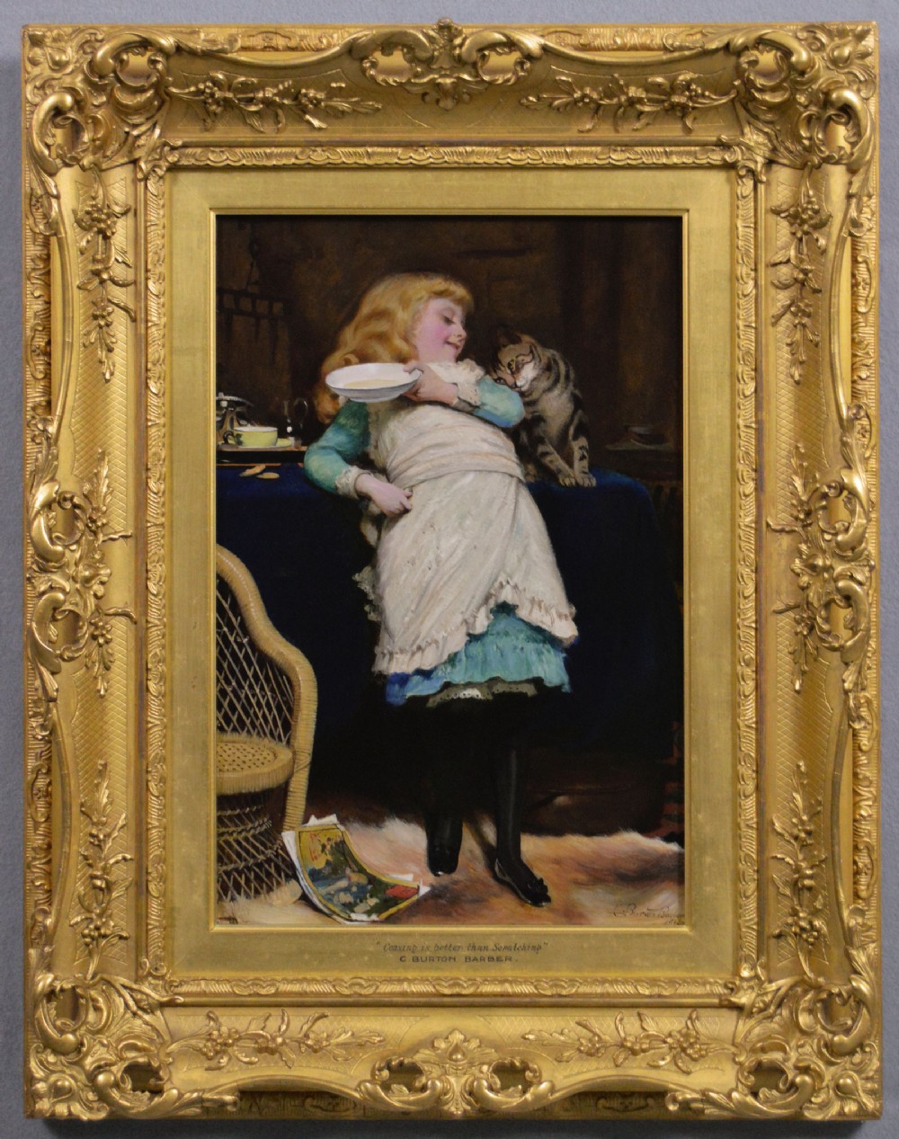 A 19th-century framed oil painting depicting a young girl in a white apron offering a saucer to a tabby cat beside a table.