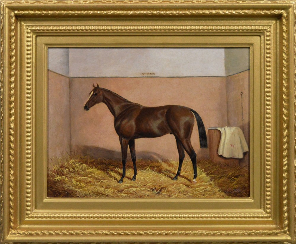 An oil painting of a brown bay racehorse standing in a straw-filled stable stall set within an ornate gold gilt frame.