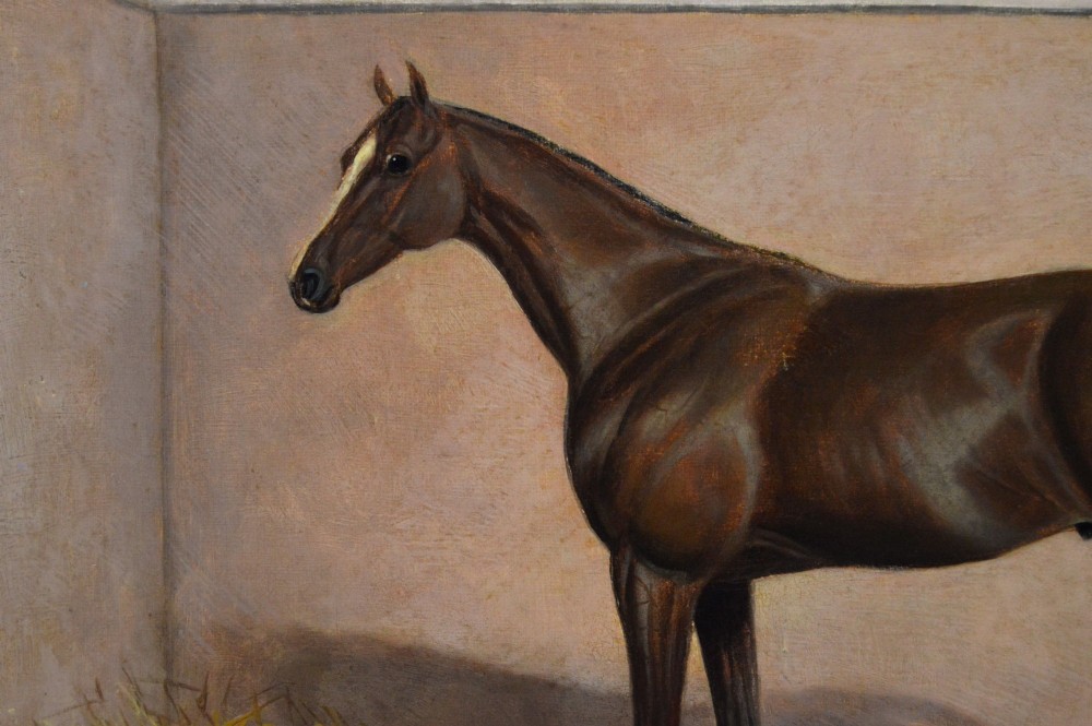 An oil painting of a brown bay racehorse standing in a straw-filled stable stall set within an ornate gold gilt frame. View III