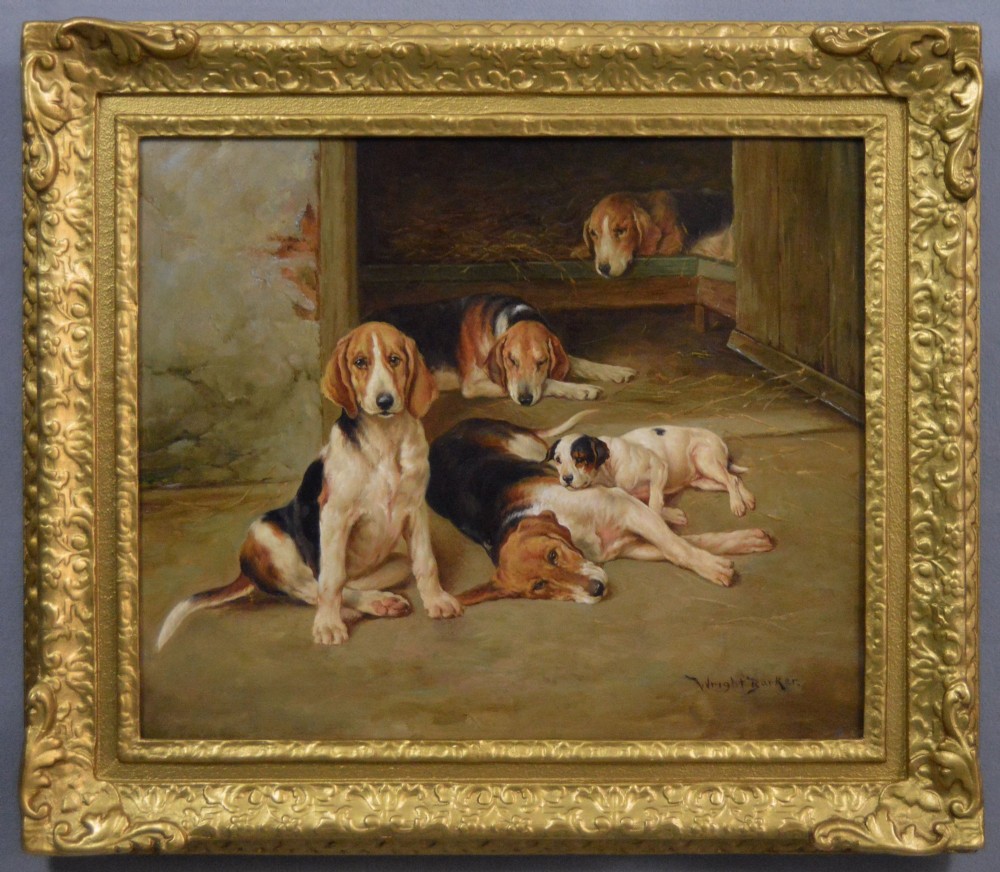 An oil painting depicting several foxhound puppies and a fox terrier resting on a barn floor, set within a heavy carved gilded frame.