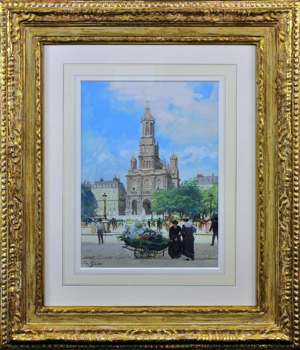 A framed antique French painting portraying a bustling Parisian square with figures, a flower cart, and a tall church against a blue sky, set within an ornate carved gold frame.