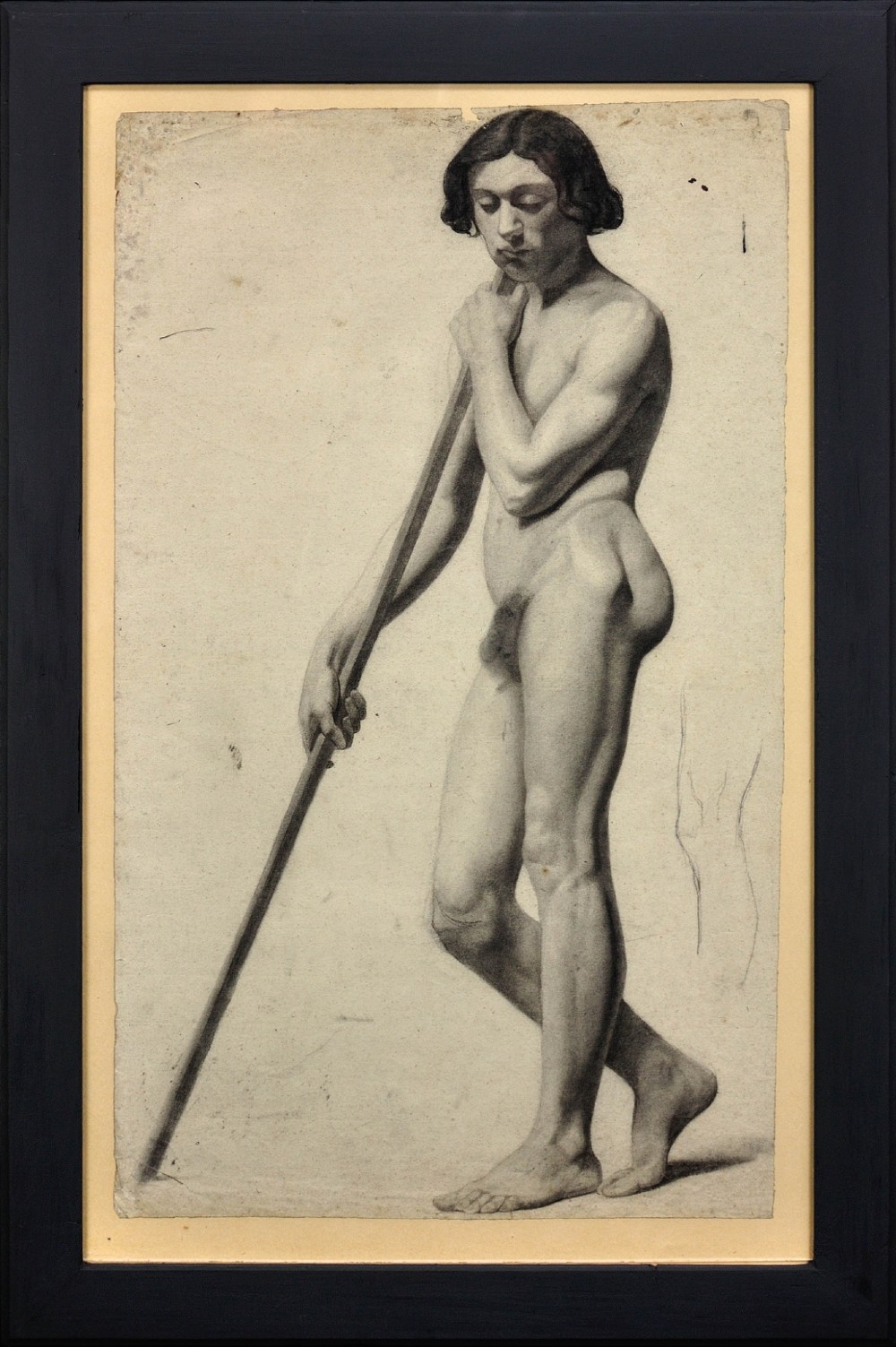 A nineteenth-century framed charcoal drawing on light cream paper depicting a full-length standing male nude holding a long staff.