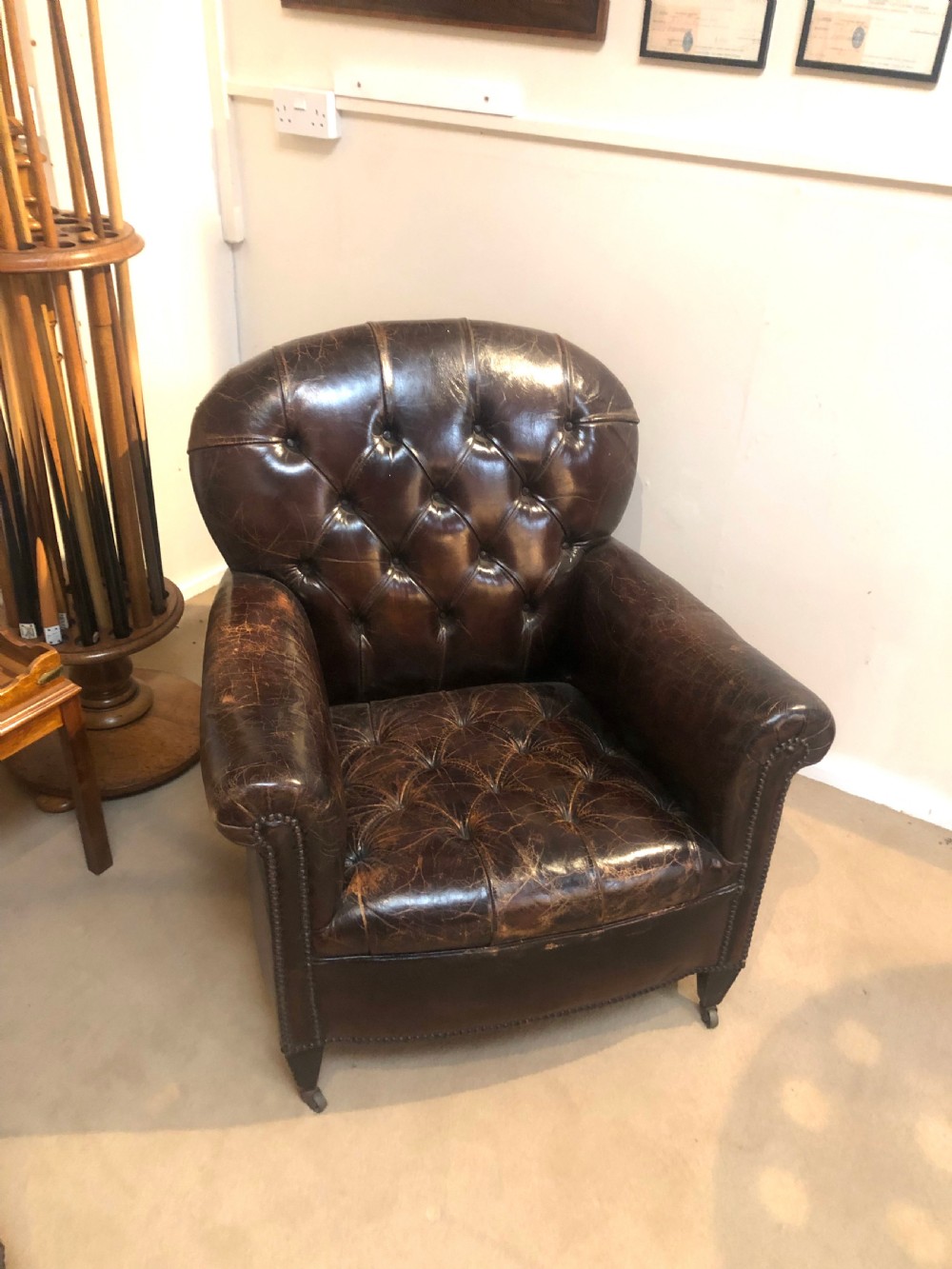 A pair of dark brown leather Edwardian club chairs featuring deep-buttoned backrests, brass stud trimming, and square tapered legs on castors. View III