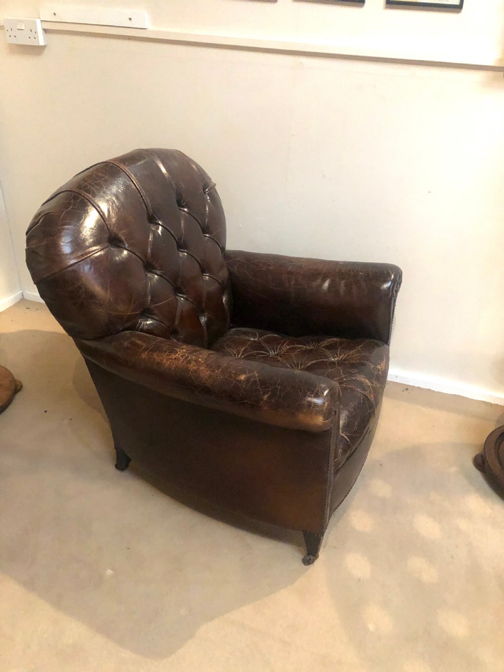 A pair of dark brown leather Edwardian club chairs featuring deep-buttoned backrests, brass stud trimming, and square tapered legs on castors. View V