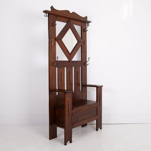 fig 1. An Arts and Crafts oak hallstand featuring a diamond-shaped mirror frame, integrated brass coat hooks, turned spindles, and a seat with lift-top storage.