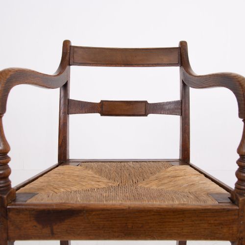 fig 2. A pair of 1820s Georgian dark oak elbow chairs featuring woven rush seats, swept armrests, and turned front legs.
