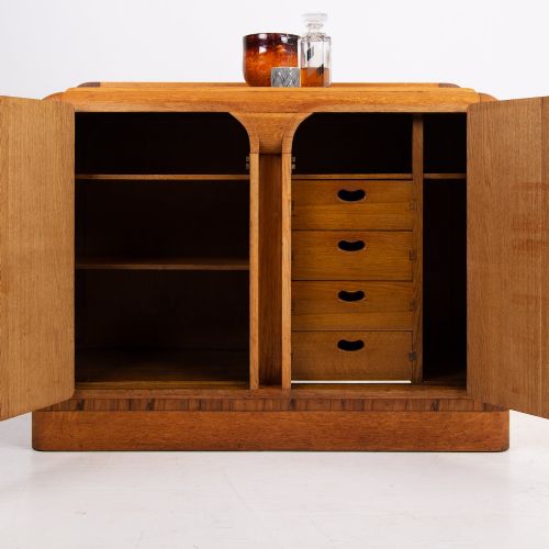 fig 1. An Art Deco golden oak sideboard cabinet featuring rounded top edges, quarter-sawn wood grain, two central doors with wooden block handles, and a solid base plinth.