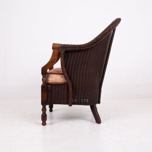 fig 2. A 1930s dark brown Lloyd Loom woven armchair featuring carved oak armrests, turned front legs, and a patterned seat cushion.