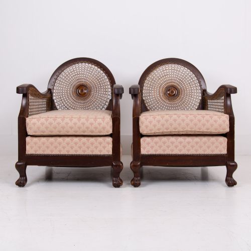 fig 1. A pair of 1920s dark wood bergere armchairs featuring circular woven cane backs, cane sides, and pink fan-pattern upholstered cushions.