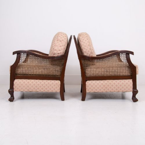 fig 2. A pair of 1920s dark wood bergere armchairs featuring circular woven cane backs, cane sides, and pink fan-pattern upholstered cushions.