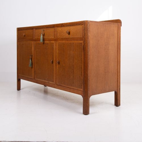 fig 1. A 1930s light oak sideboard featuring three upper drawers over three panelled cupboard doors with wooden knob handles.