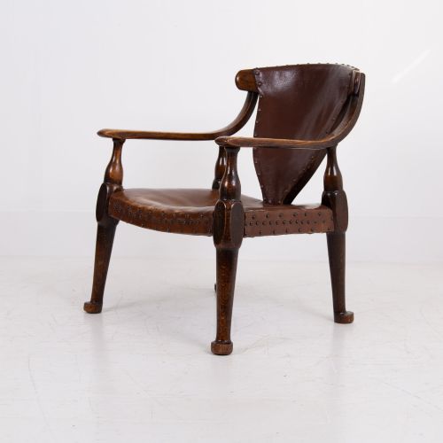 fig 2. An Arts and Crafts style dark oak armchair featuring turned front legs, wide curved armrests, and brown studded leather upholstery.