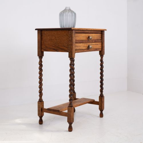 fig 1. A warm brown oak side table featuring two stacked drawers with metal shell handles, four turned barley twist legs, and a low rectangular shelf.