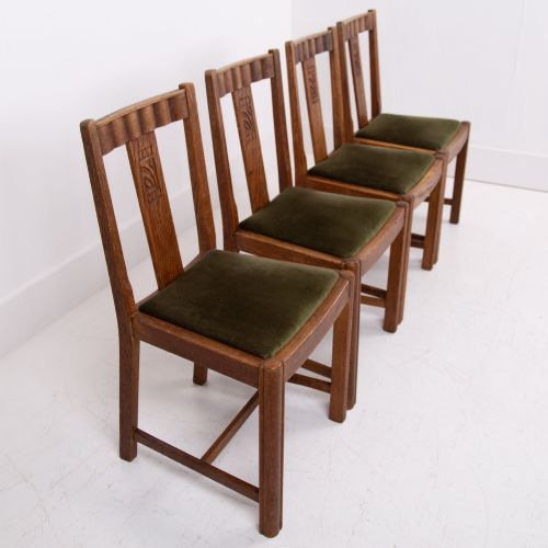 fig 1. A set of four 1930s oak dining chairs featuring carved back splats, fluted top rails, and green velvet upholstered seats.