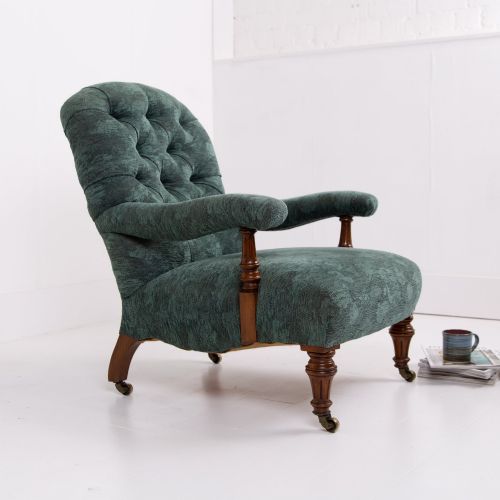 fig 1. A profile view of a Victorian walnut open library armchair with dark green button-backed upholstery, turned front legs, and brass castors.