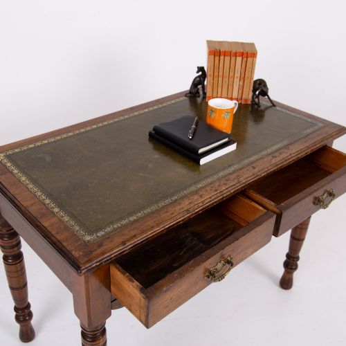 fig 1. A brown walnut writing desk featuring two frieze drawers with brass handles, turned legs, and a rectangular inset leather top.