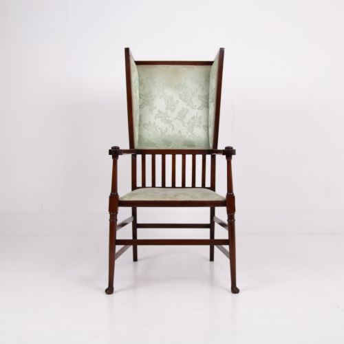 fig 1. An Arts and Crafts high-backed armchair crafted from dark timber with vertical under-arm slats, architectural wings, and pale green patterned fabric upholstery.