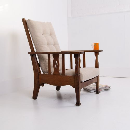 fig 1. An Arts and Crafts oak reclining armchair featuring a beige buttoned cushion and pierced side splats.